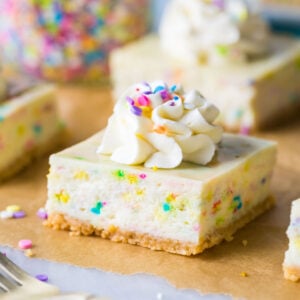 funfetti cheesecake bar topped with whipped cream and sprinkles on brown parchment