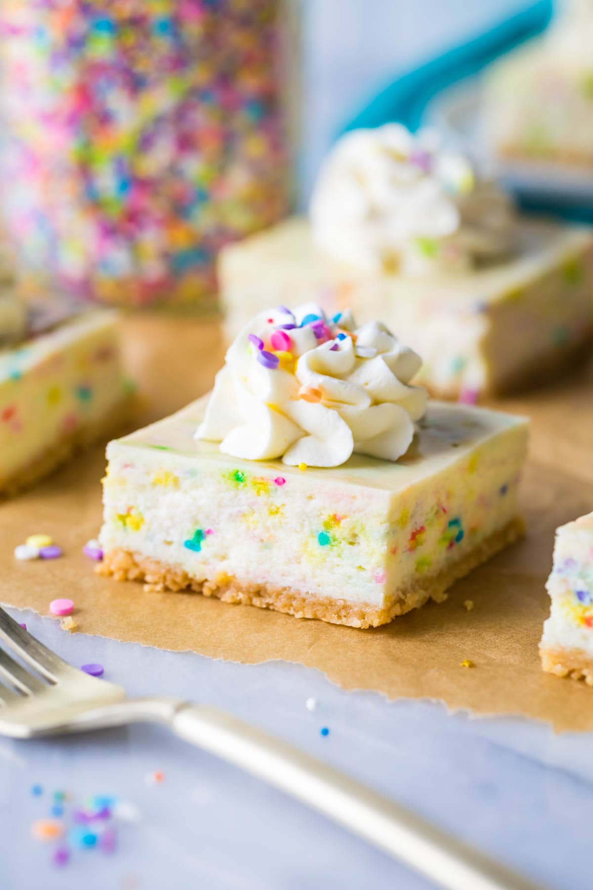 funfetti cheesecake bar topped with whipped cream and sprinkles on brown parchment