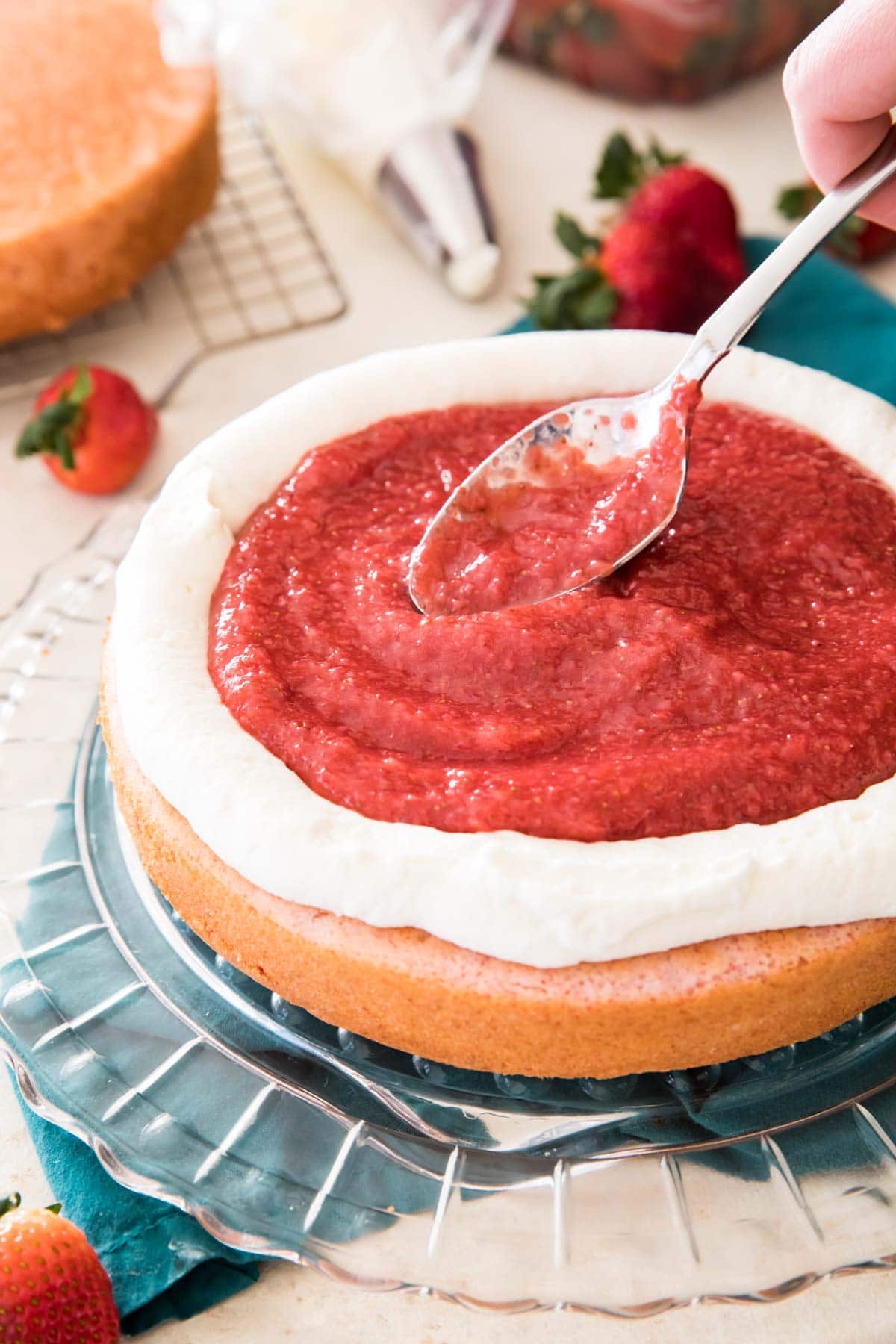 spooning strawberry jam into frosting dam on strawberry cake layer