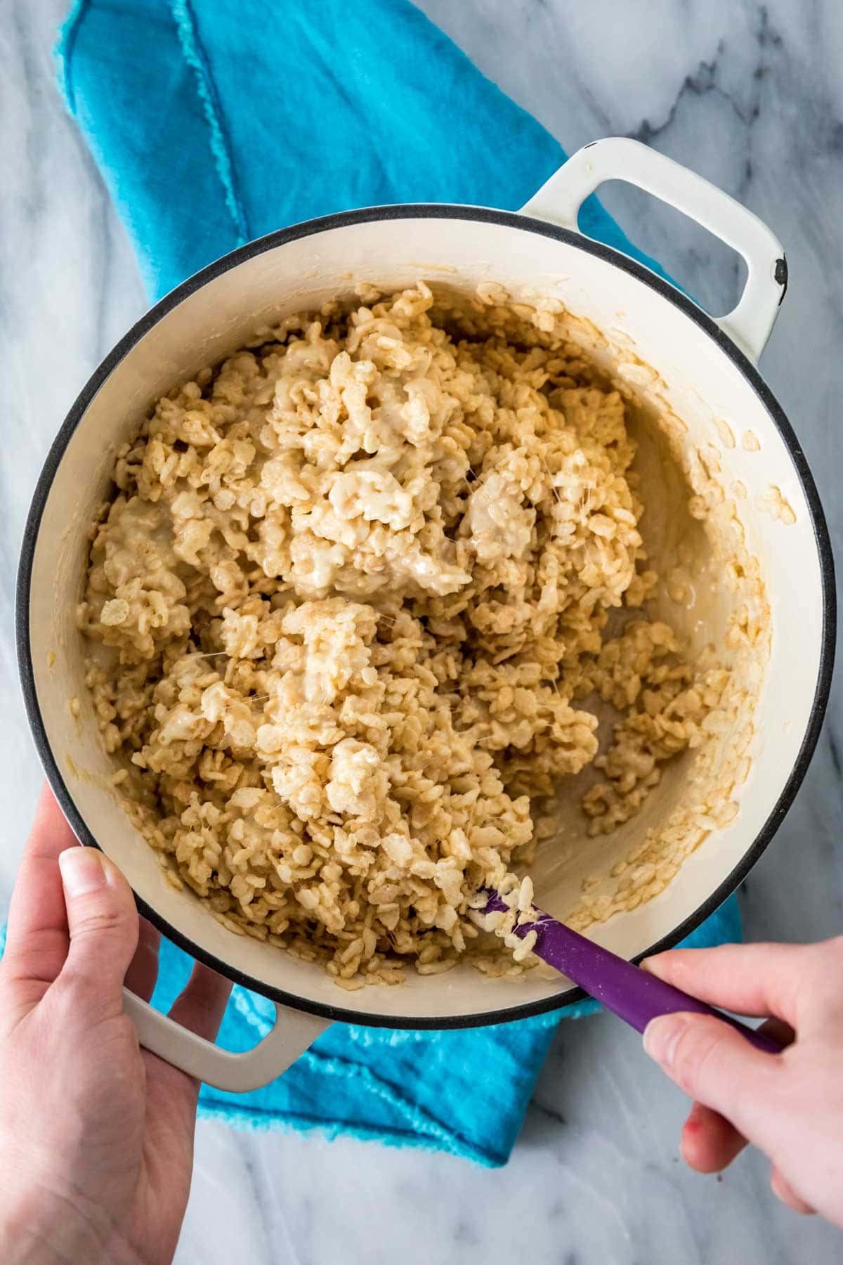 mixing cereal into a salted caramel sauce in a white Dutch oven