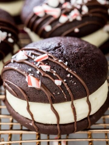 peppermint bark whoopie pies drizzled with chocolate and topped with crushed candy canes on gold metal cooling rack