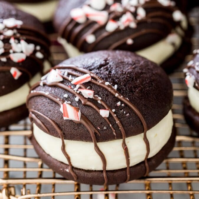 peppermint bark whoopie pies drizzled with chocolate and topped with crushed candy canes on gold metal cooling rack