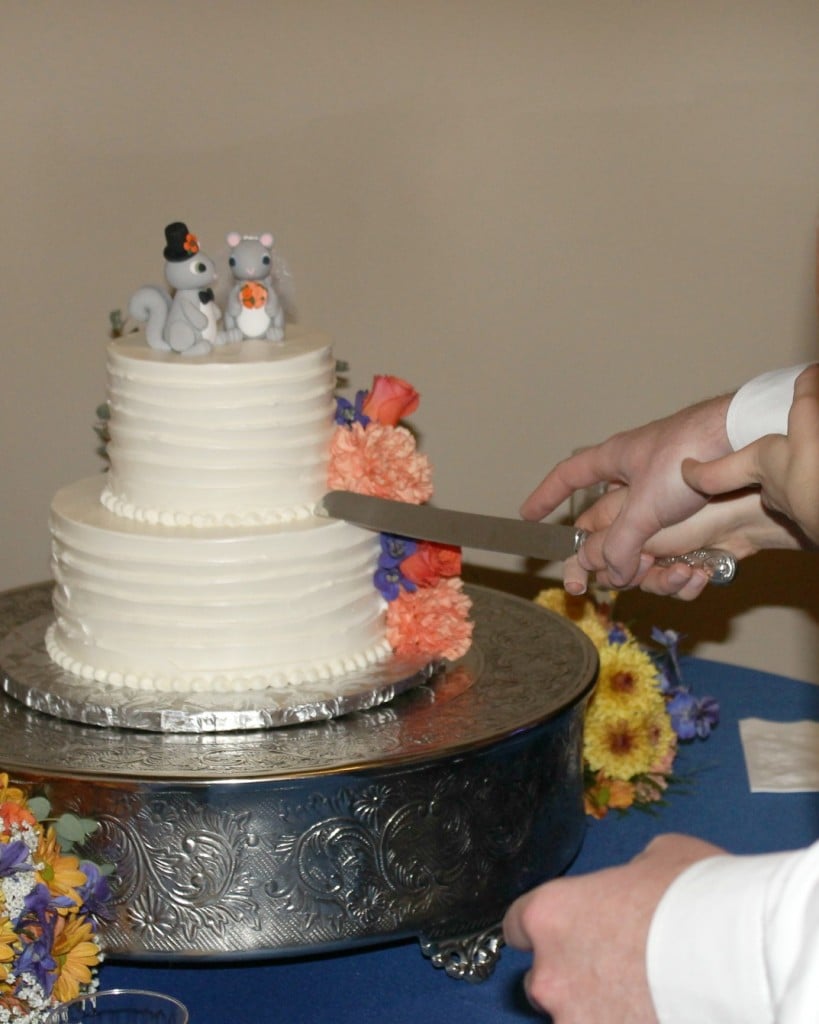 Slicing into a two tier wedding cake with squirrel bride and groom cake toppers