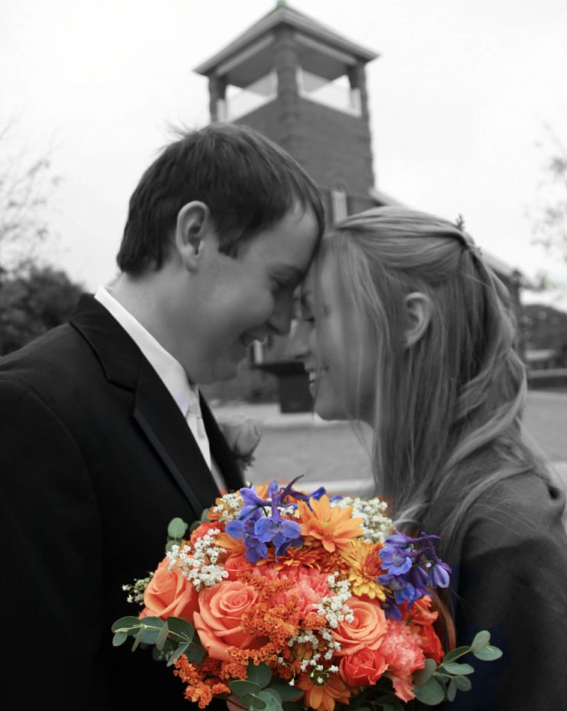 bride and groom in black and white with flower bouquet in color in foreground