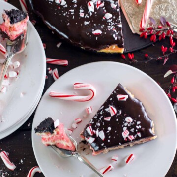 Slice of candy cane mint cheesecake on a plate with the entire cake in the background