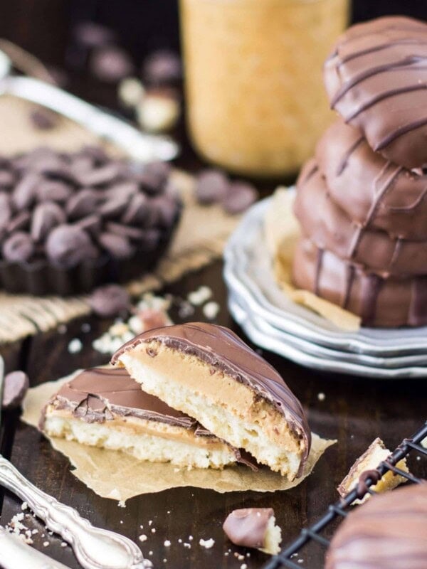 Tagalong cookies broken in half to show the layered cookie, stack of four cookies on a silver plate in the background