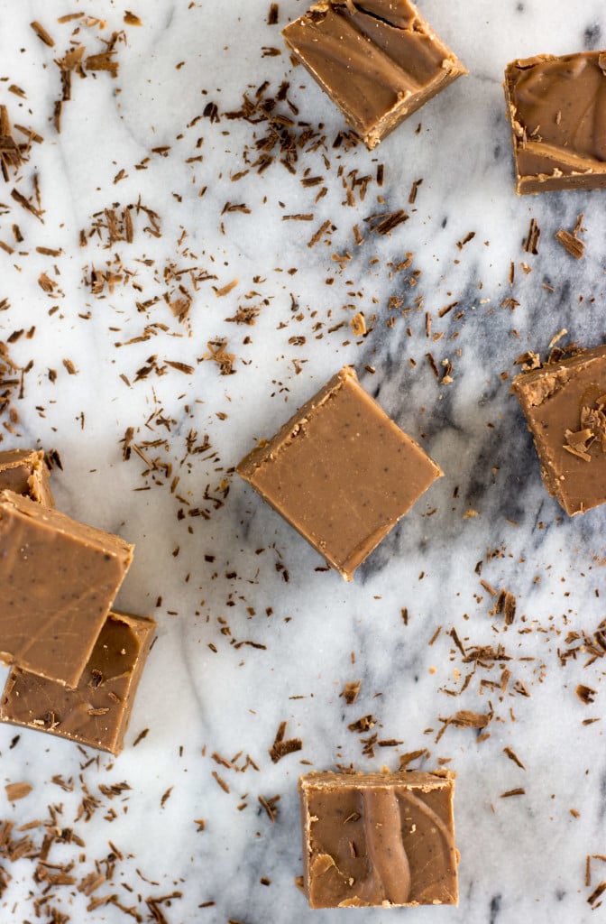 Overhead of old-fashioned chocolate fudge that's been cut into squares. On marble board surrounded by chocolate shavings.