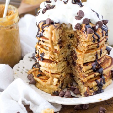 Tall stack of Stack of peanut butter chocolate chip pancakes, drizzled with chocolate sauce and topped with whipped cream and chocolate chips