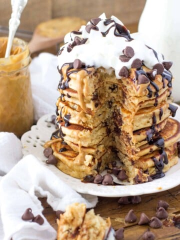 Tall stack of Stack of peanut butter chocolate chip pancakes, drizzled with chocolate sauce and topped with whipped cream and chocolate chips