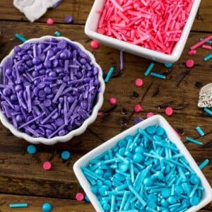 Three bowls: one filled with blue sprinkles, one with pink sprinkles, one with purple sprinkles