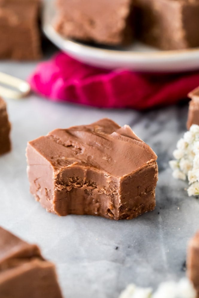 Square of chocolate fudge with a bite out of it on marble board. Showing creamy interior.