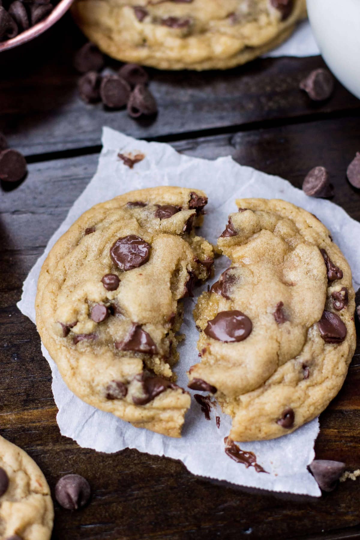 Overhead of the worst chocolate chip cookie on parchment paper on a wood surface, broken in half