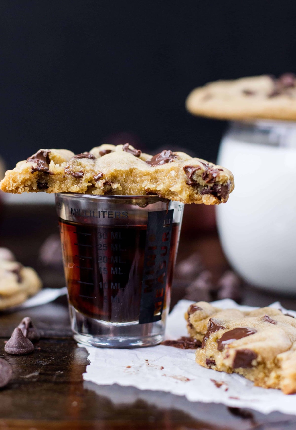 chocolate chip cookie broken in half to show the inside, perched on a shotglass filled with the secret ingredient (maple syrup)