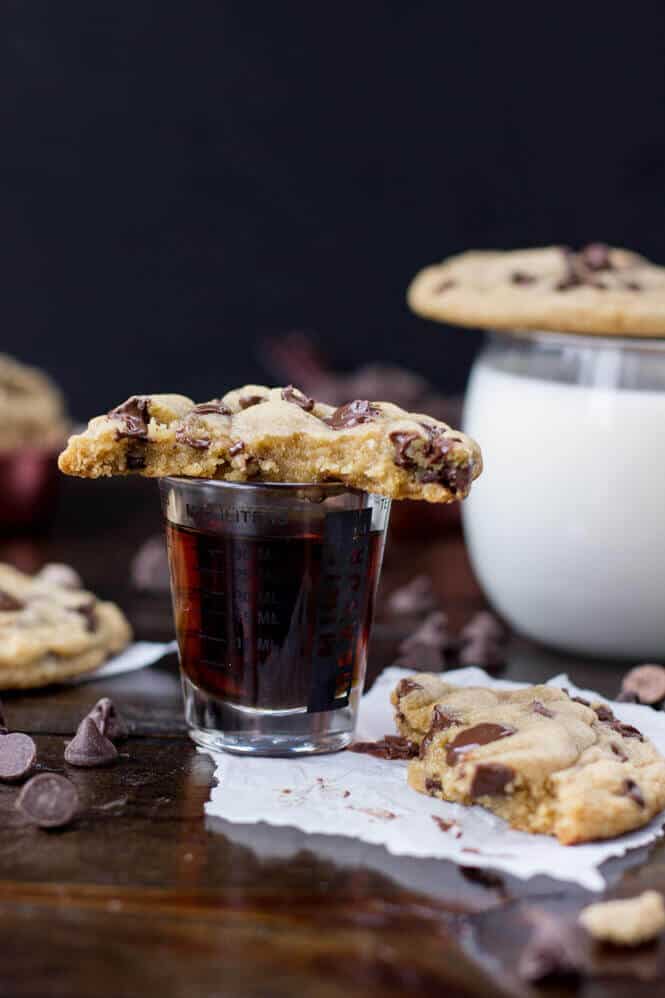 chocolate chip cookie broken in half, sitting on a measuring cup filled with maple syrup