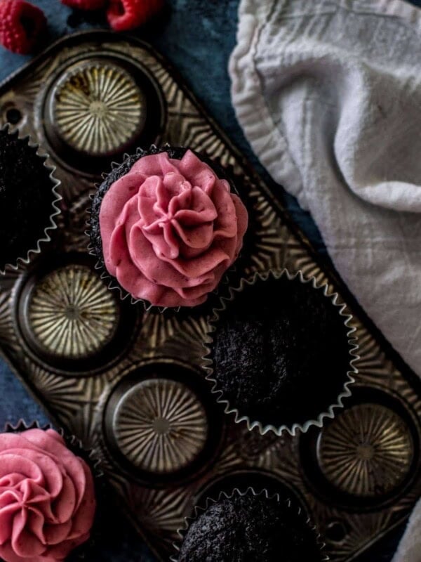 Overhead shot of dark chocolate cupcakes, some with raspberry frosting, sitting on a cupcake pan