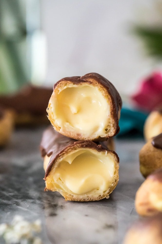 Chocolate eclair cut in half and stacked on top itself -- showing pastry cream filled interior