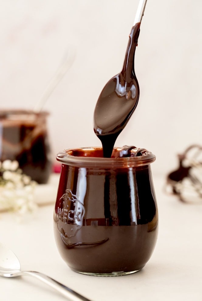 Spooning hot fudge sauce out of a jar, showing thick consistency.