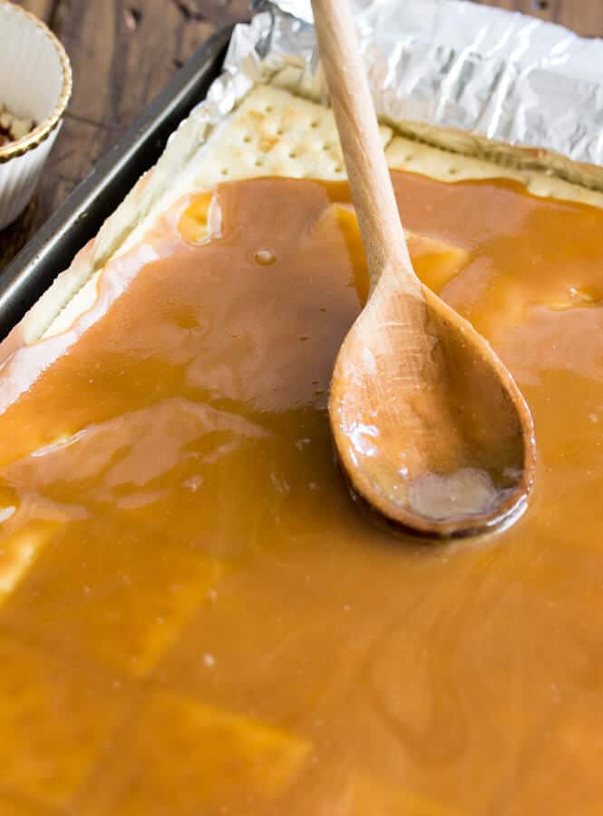 Wooden spatula spreading caramel mixture over saltine crackers