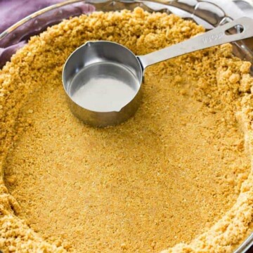 Graham cracker crust being pressed in to glass pie plate