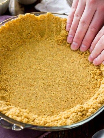 Hands pressing graham cracker crust in to pie plate