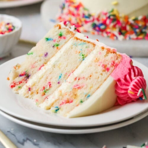 Slice of funfetti cake on a plate with the remaining cake in the background.