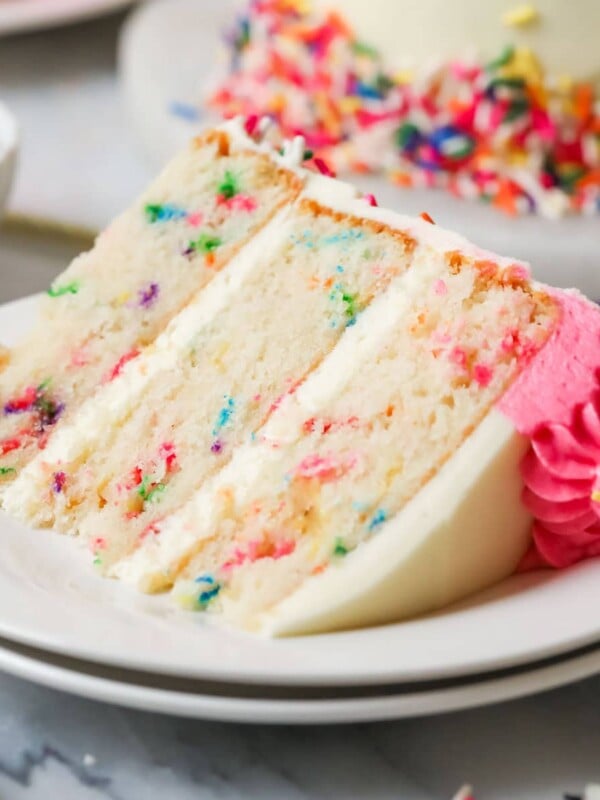 Slice of funfetti cake on a plate with the remaining cake in the background.