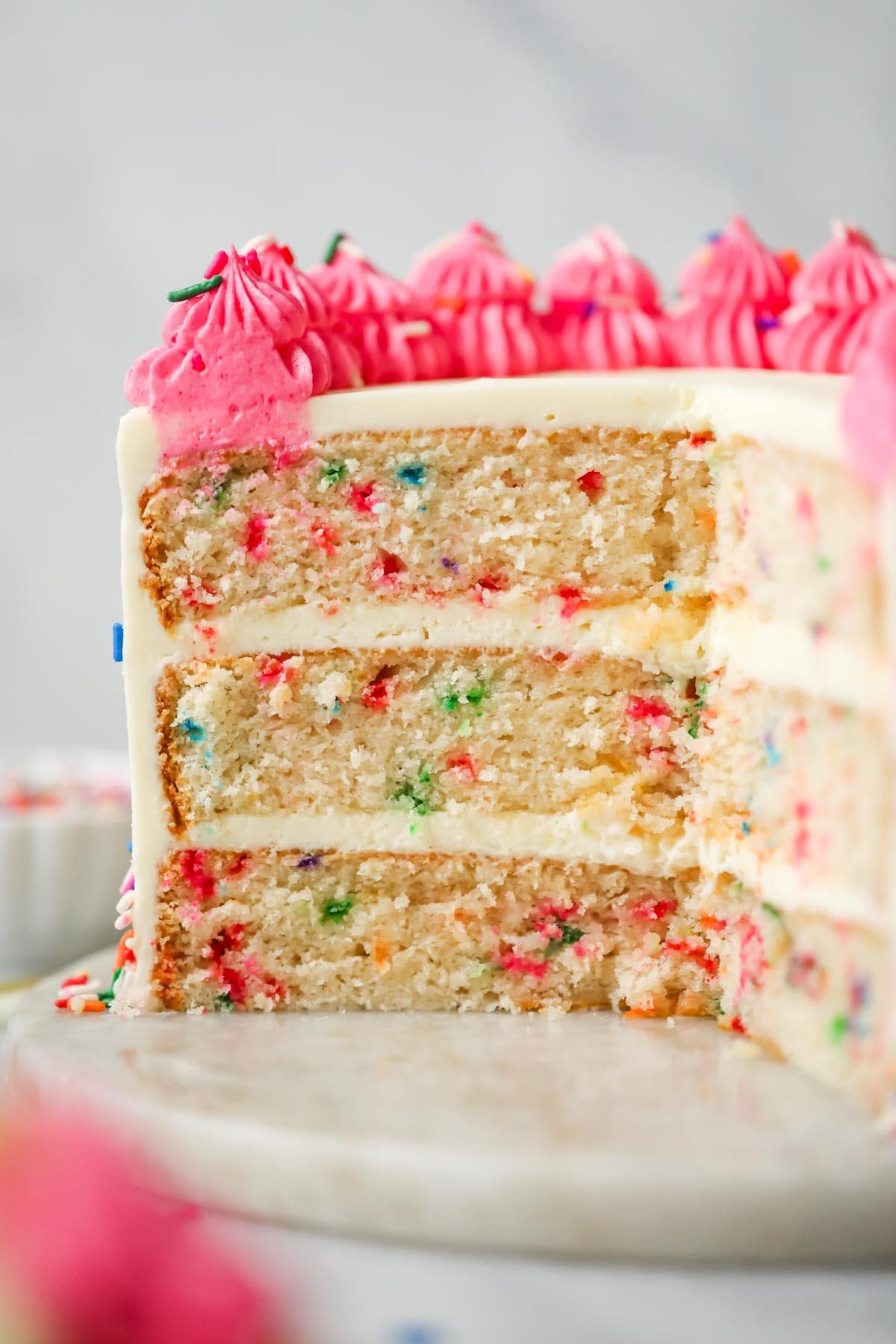 Cross section of a three-layer cake made with sprinkles and a bright pink frosting border.