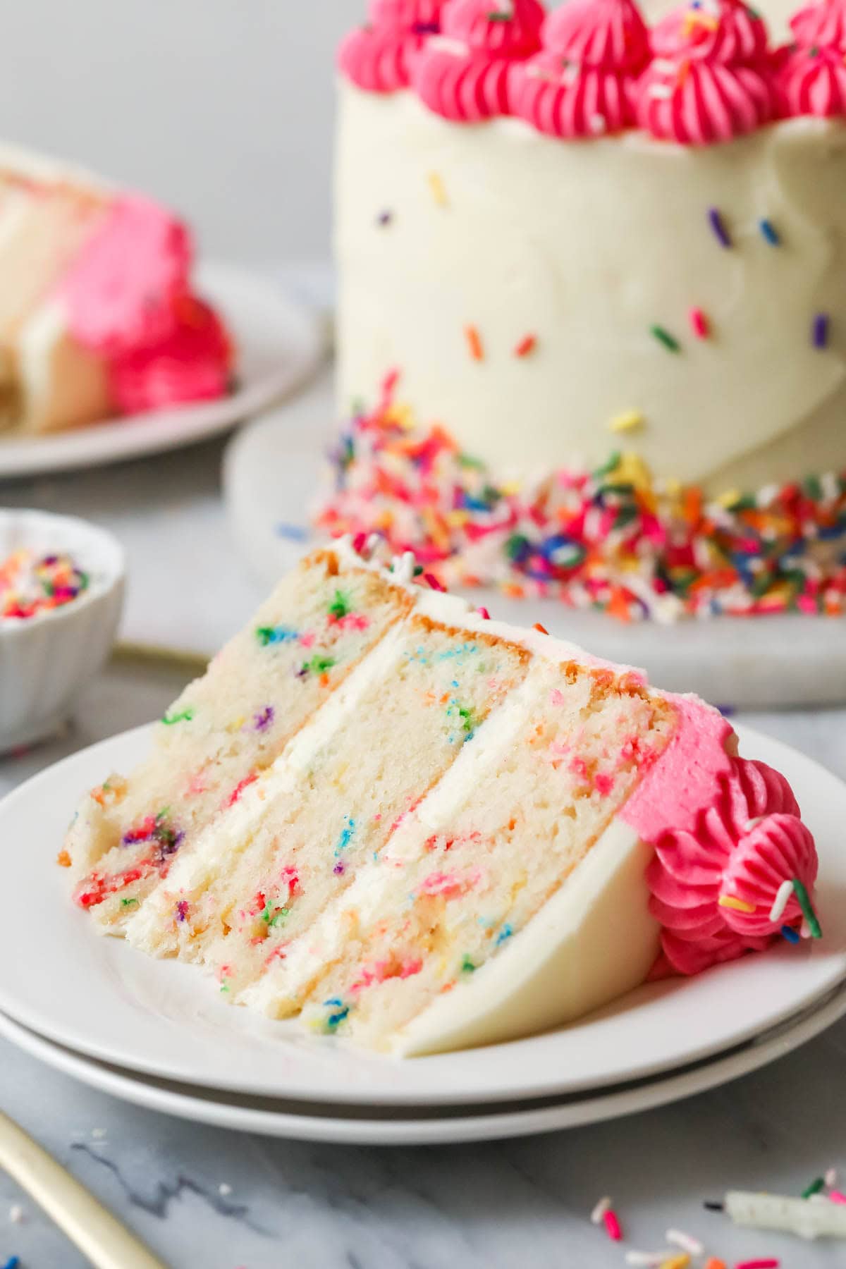 Slice of funfetti cake on a plate with the remaining cake in the background.