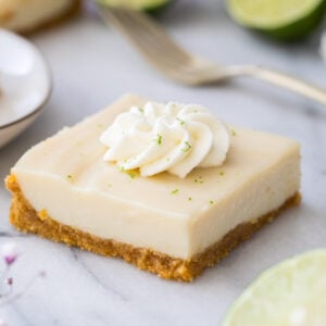 square of creamy key lime pie bar on marble, topped with whipped cream and lime zest