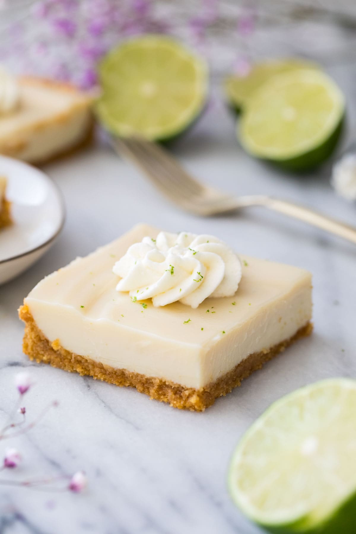 square of creamy key lime pie bar on marble, topped with whipped cream and lime zest