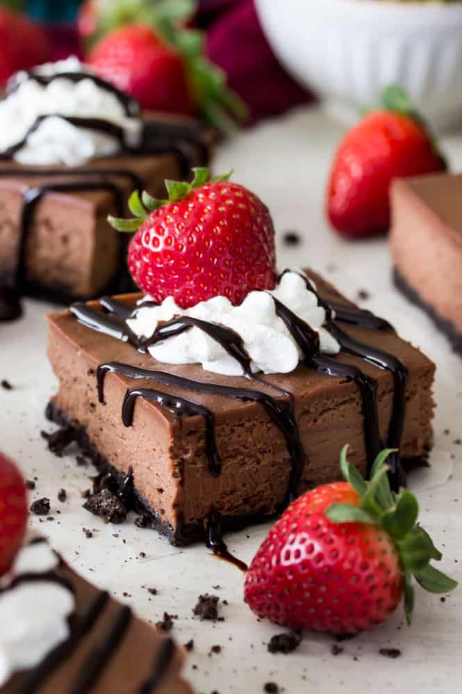 Chocolate cheesecake bar, drizzled with chocolate, topped with whipped cream and a strawberry