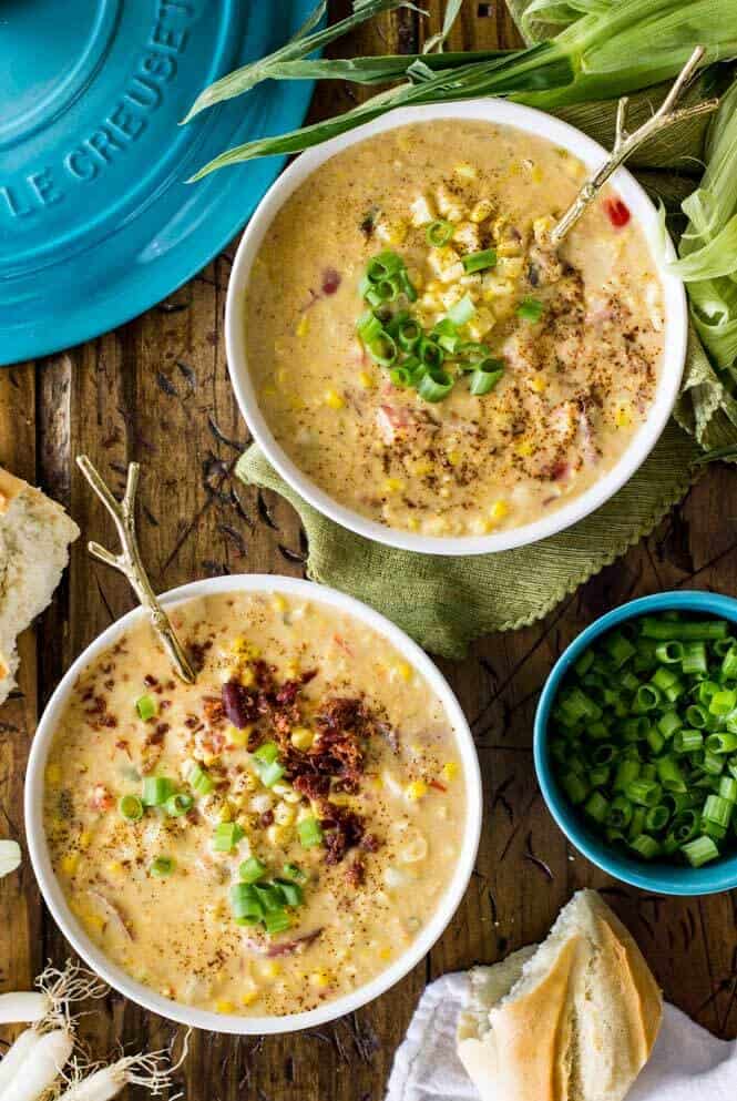 Two bowls of summer corn chowder garnished with chives and bacon