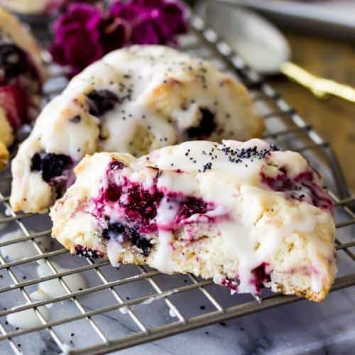 Triple berry scones drizzled with glaze on cooling rack