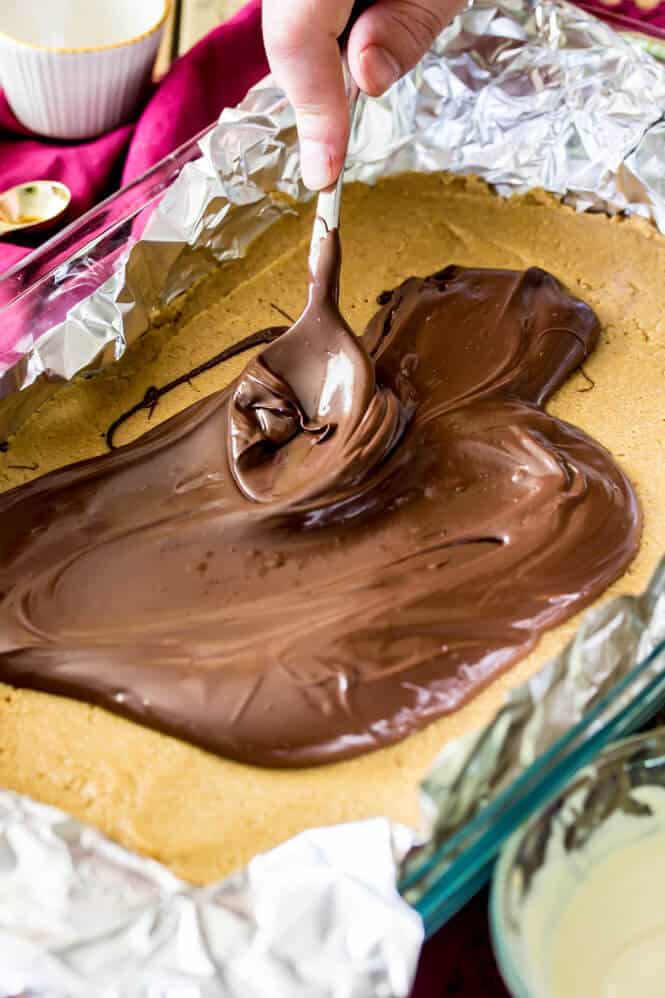 Smoothing melted chocolate over the top of peanut butter bars