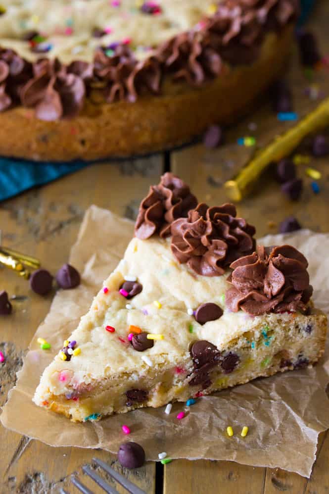 A slice of chocolate chip cookie cake with sprinkles and chocolate frosting