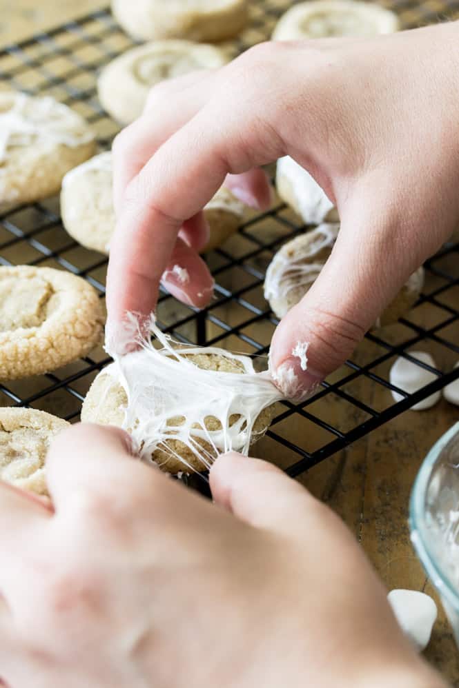 Hands stretching marshmallow over cookie to make spiderweb