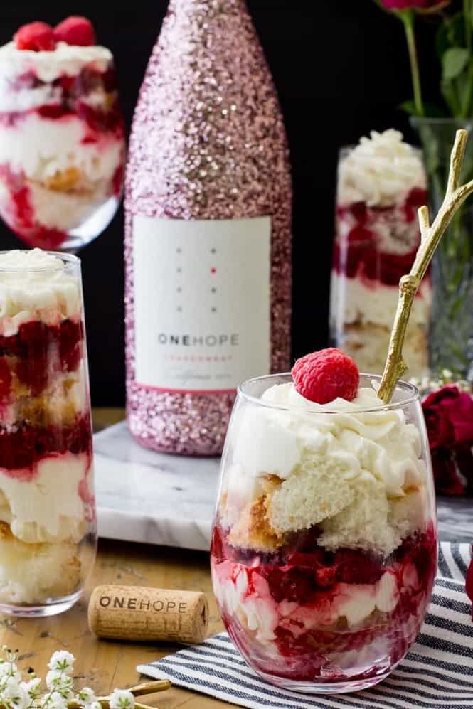 trifle in stemless wine glass with raspberry on top. glittery pink bottle in background