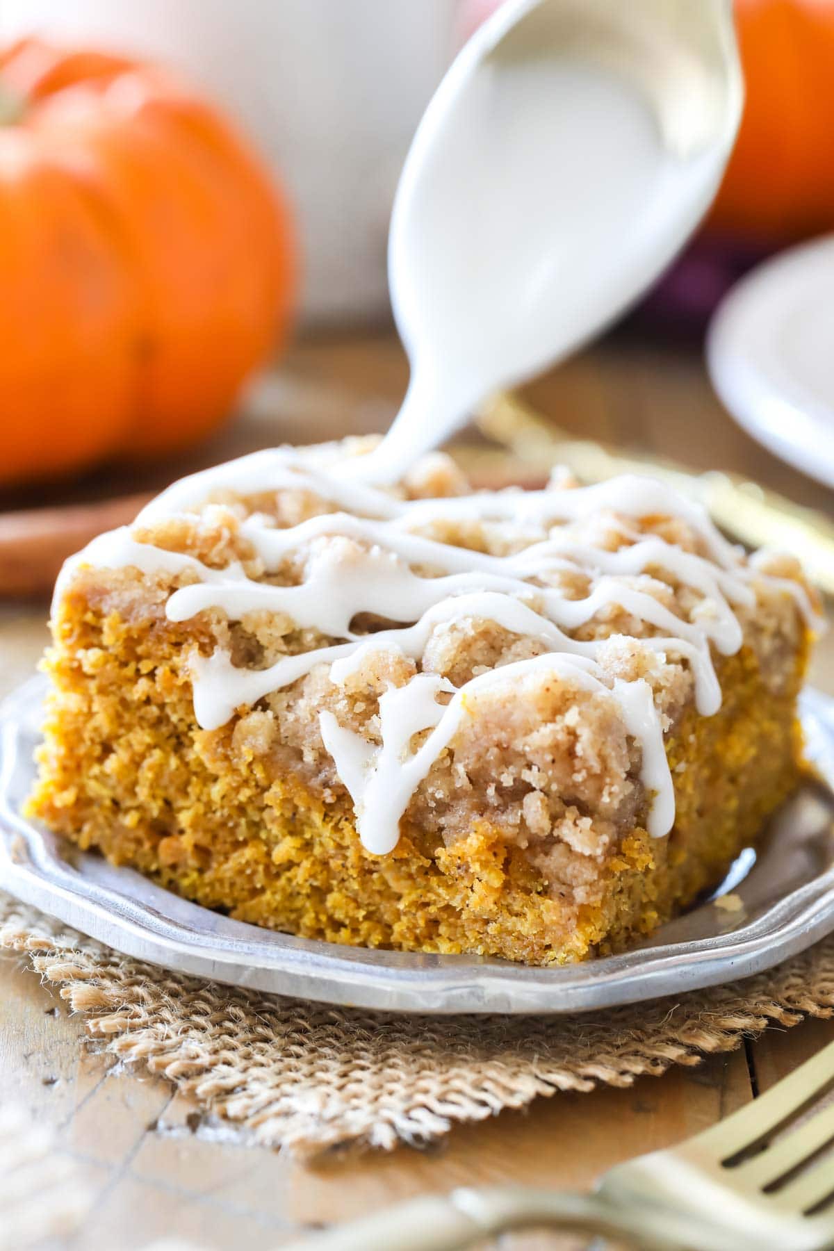 drizzling vanilla glaze over a plated square of pumpkin coffee cake