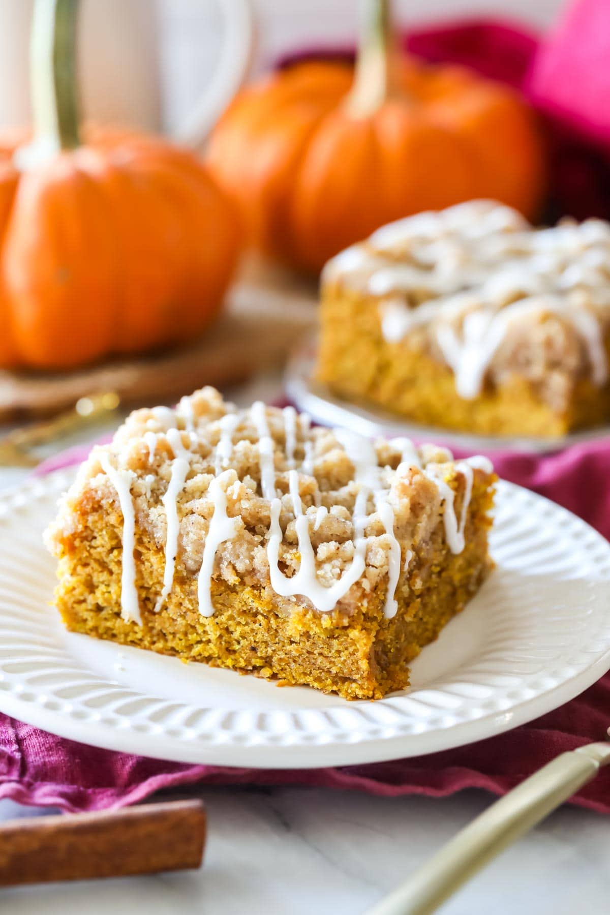 square of pumpkin crumb cake on white plate with pumpkins and more crumb cake in background