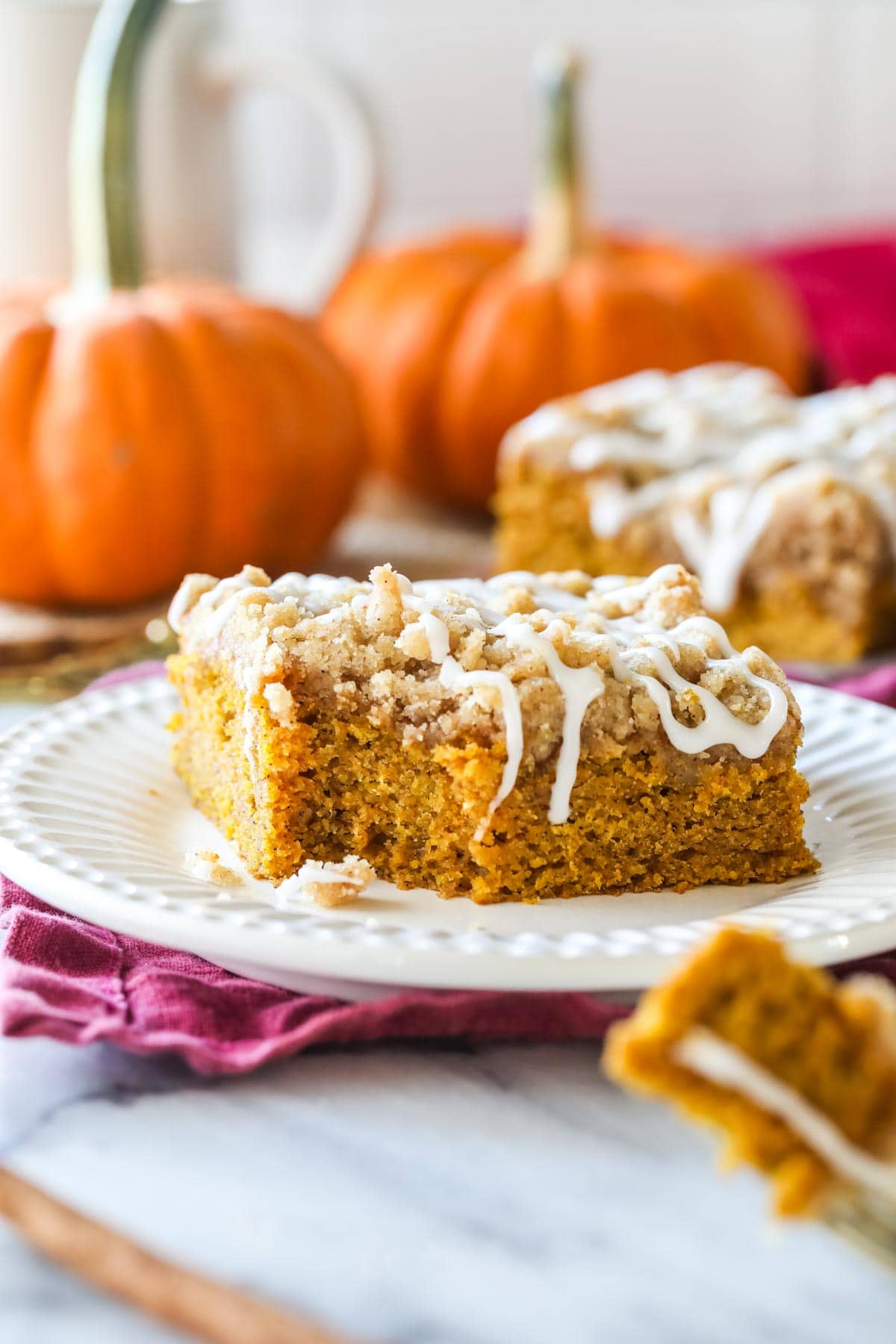 Slice of pumpkin coffee cake with a forkful missing. pumpkins in background