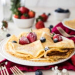 folded crepes with powdered sugar and strawberries on a white plate