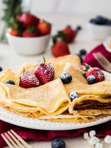 folded crepes with powdered sugar and strawberries on a white plate