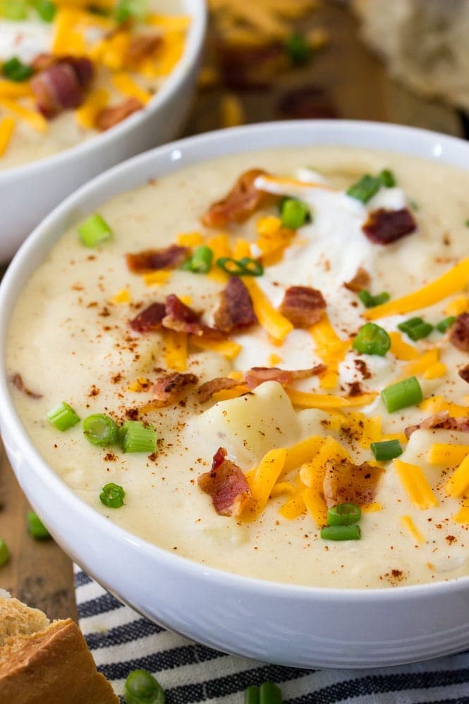 A close up view of creamy potato soup, topped with bacon, sour cream, chives, and cheddar cheese
