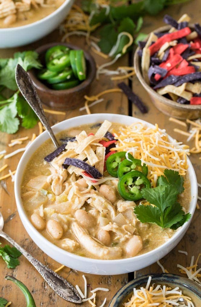 A bowl of white chicken chili topped with chips, jalapenos, cilantro, and shredded cheese