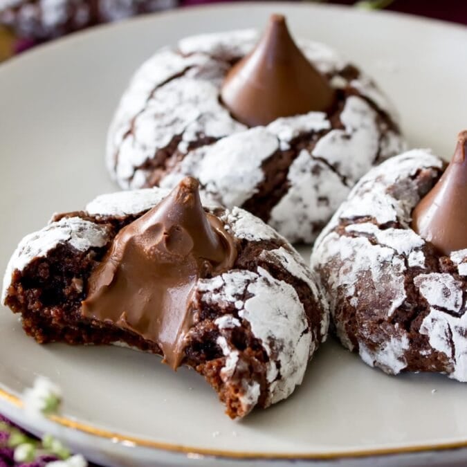 three chocolate blossom cookies on a white plate. Front cookie has a bite out of it exposing melty center.