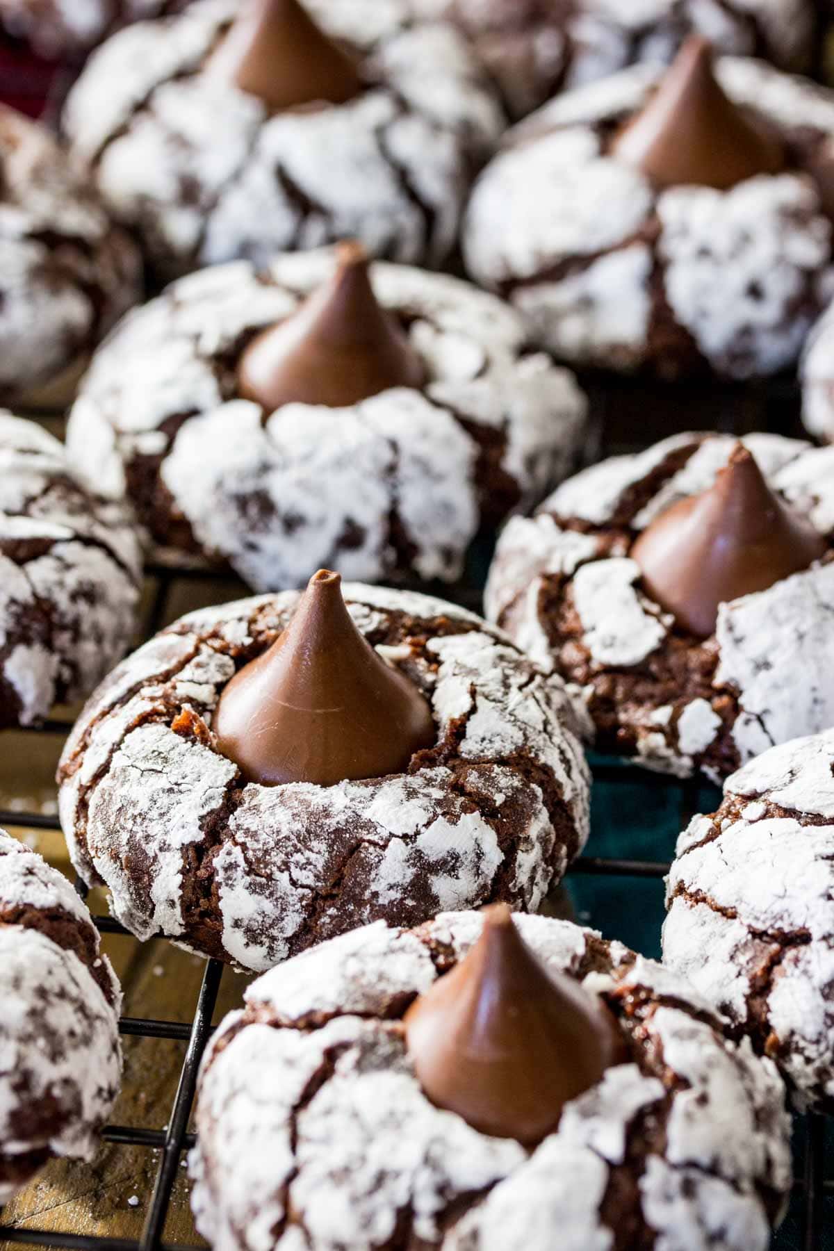 Powdered sugar covered chocolate cookies topped with chocolate kisses arranged on cooling rack