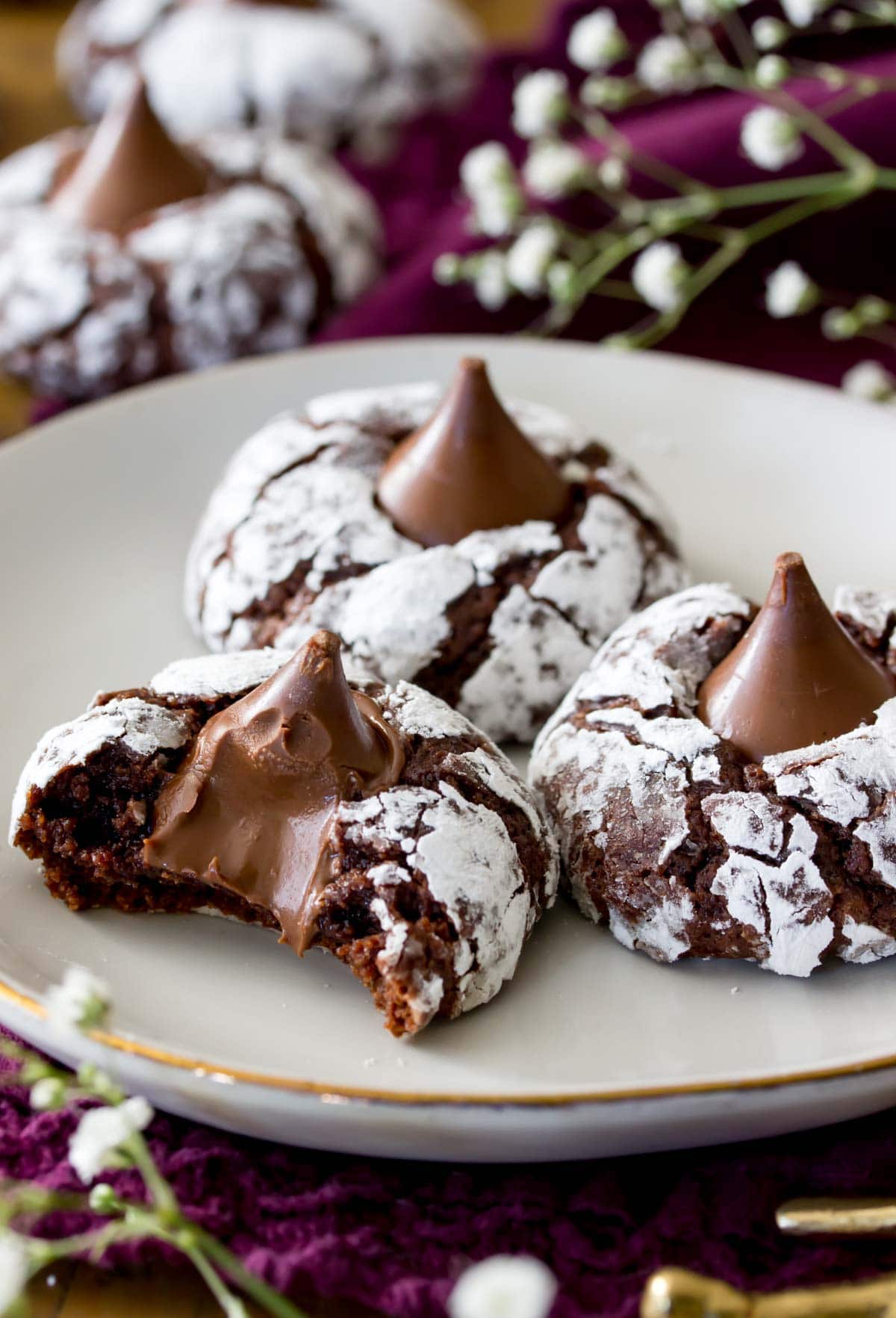 three chocolate blossom cookies on a white plate. Front cookie has a bite out of it exposing melty center.