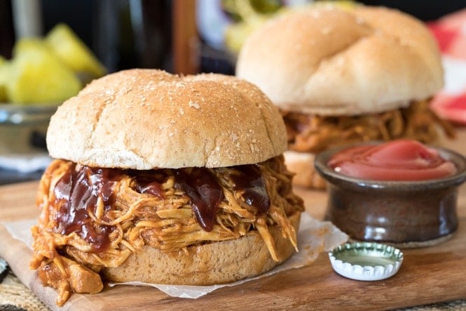 BBQ Pulled Chicken sandwich on a wooden platter beside a ketchup dish