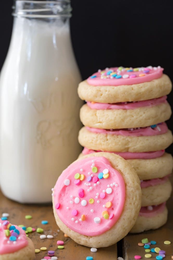 A stack of soft frosted sugar cookies beside a bottle of milk