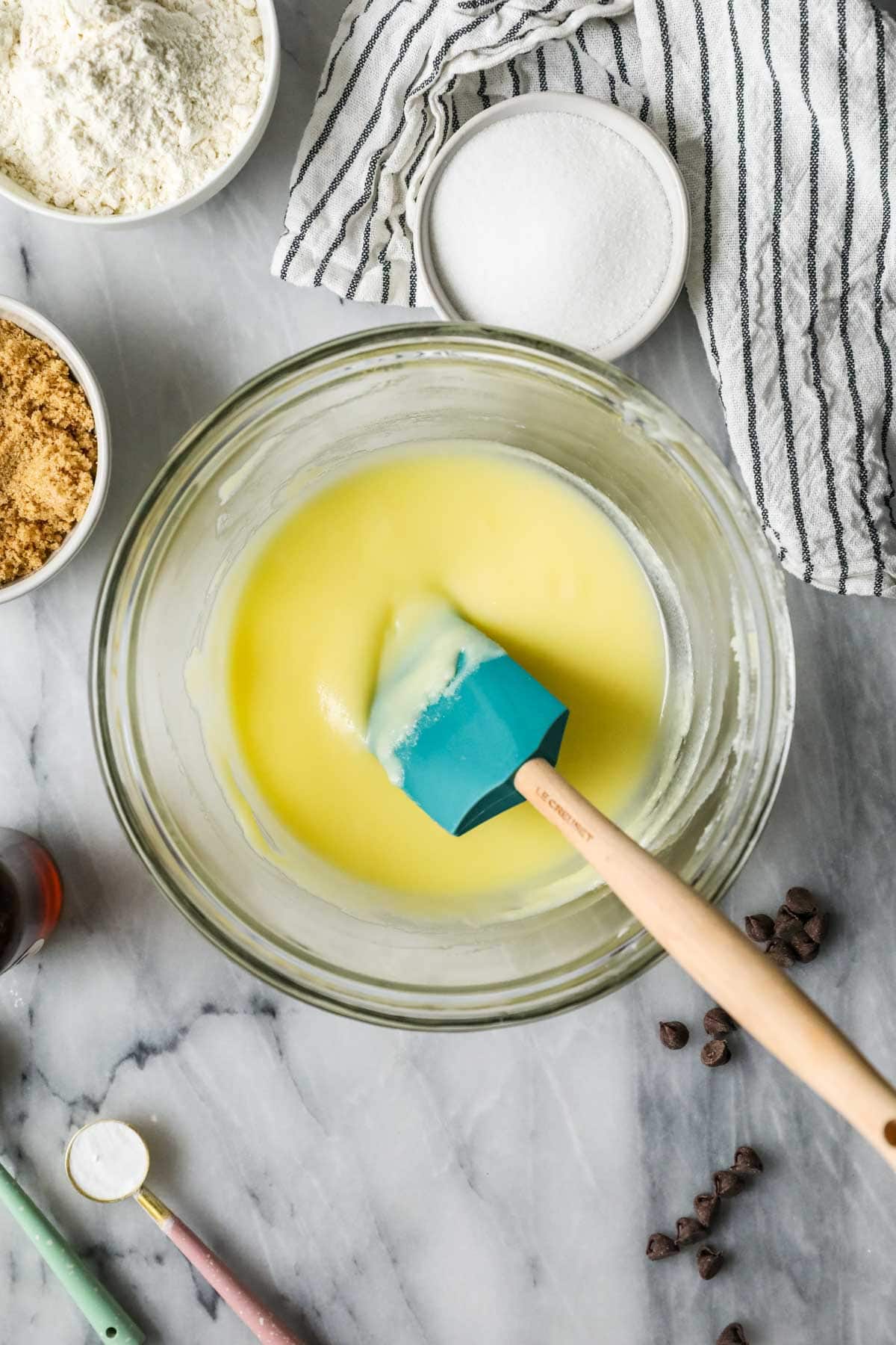 melted butter in a glass mixing bowl, surrounded by various ingredients and a striped blue and white towel.